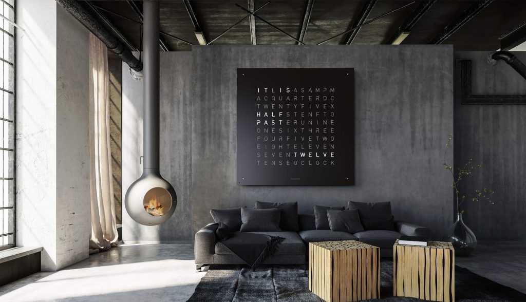 QLOCKTWO One Hundred Eighty in black on a dark colored wall with a sofa in front of it and two small coffee tables in front of the sofa