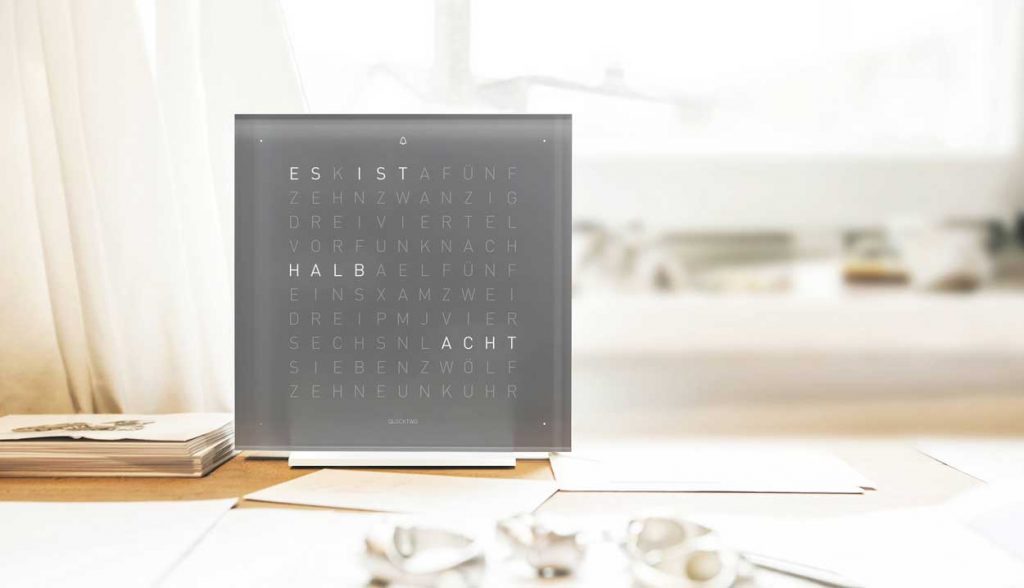QLOCKTWO Touch in grey on a light wooden desk with a sunny window behind