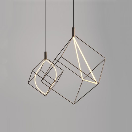 Pair Spectrum lights hanging from the ceiling. One has a triangular bulb in the middle of the cube frame and the other has an oval bulb in the middle of the cube frame in front of a white background