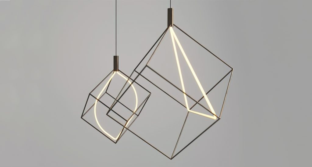 Pair Spectrum lights hanging from the ceiling. One has a triangular bulb in the middle of the cube frame and the other has an oval bulb in the middle of the cube frame in front of a white background