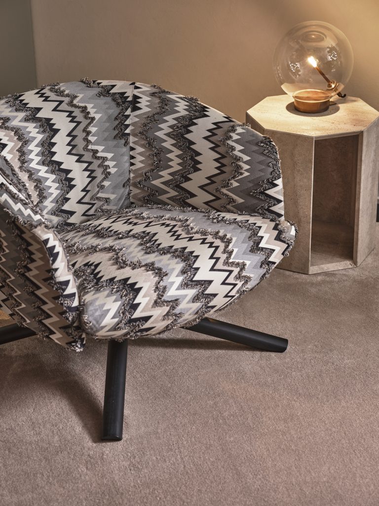 Livre Swivel in a black, white, and brown zigzag pattern on top of a cream rug with a small desk side table in the back