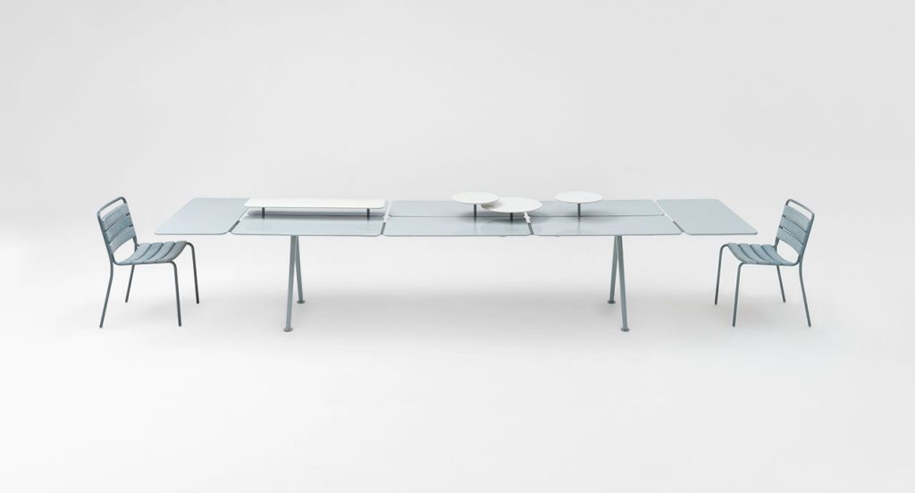Side view of Altopiano table with a chair at both ends of the table in front of a white background