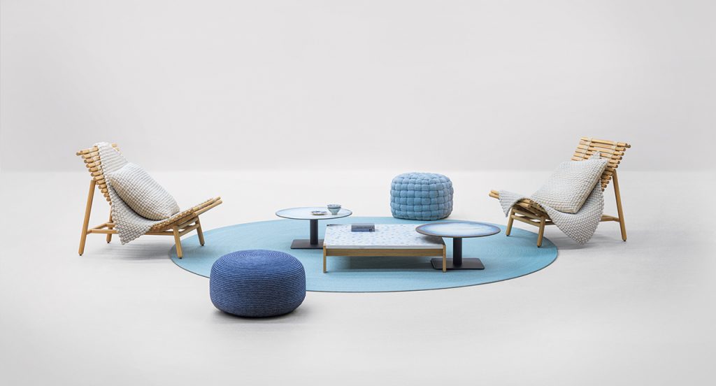Pair Shibui Armchair on both sides of a blue rug with a blue table on top of the rug and blue chairs next to the rug