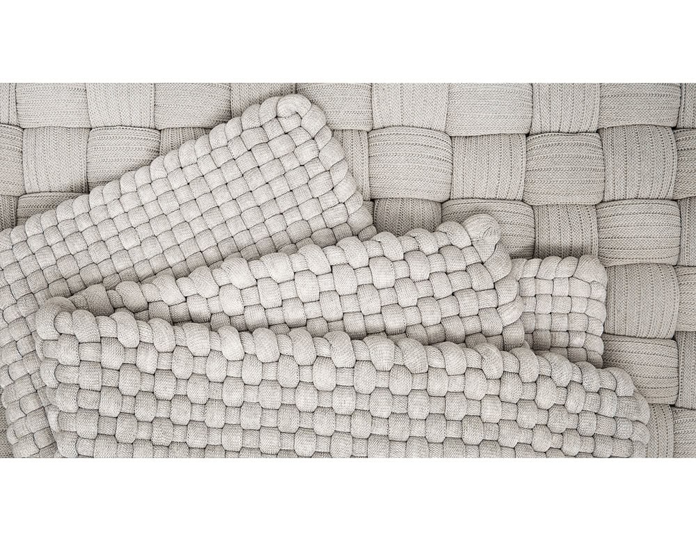 Close-up of interwoven beige fabric panels forming a textured surface, with layers of thick, soft braided padding arranged diagonally.