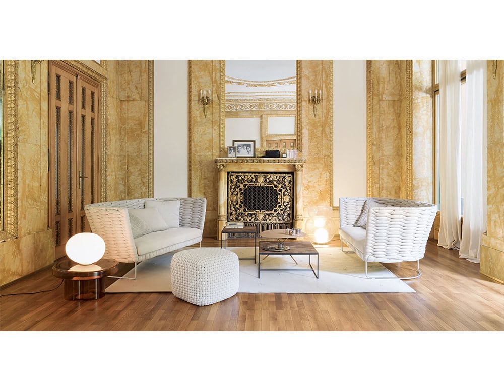 Luxurious living room with golden marble walls, ornate fireplace, and woven white sofas, complemented by a textured ottoman and modern lighting accents.