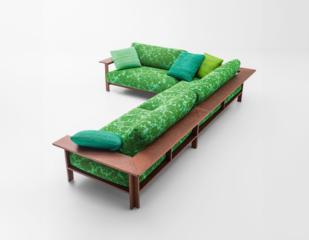 A modular outdoor sofa with a warm wooden frame and lush green upholstery, accented by gradient green cushions, forming an inviting L-shaped arrangement ideal for relaxed open-air lounging.