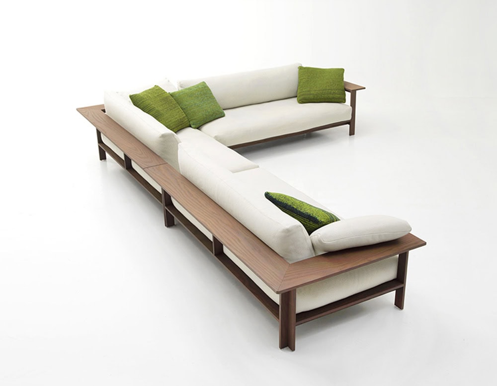 An outdoor sectional sofa with a warm wooden frame and soft cream cushions, accented by textured green pillows, creating a fresh, elegant look ideal for open-air relaxation.