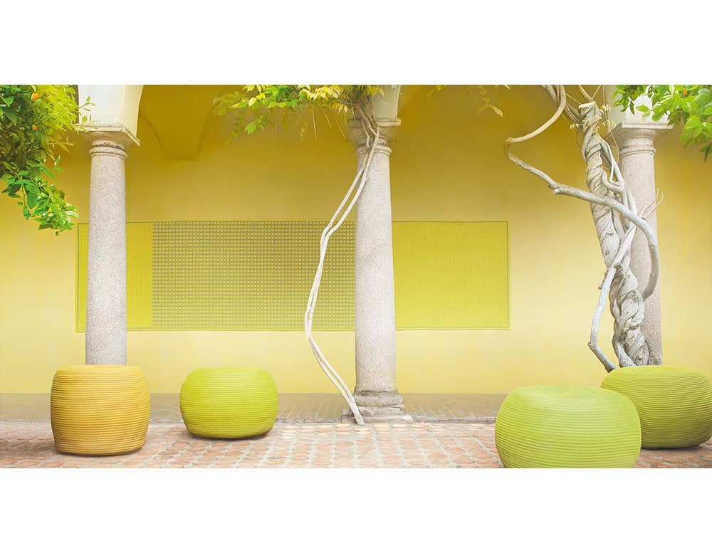 Vibrant poufs in shades of yellow and green anchor this sunlit arcade. Their soft rounded forms balance the architectural columns, bringing a touch of playful comfort to the structured setting.