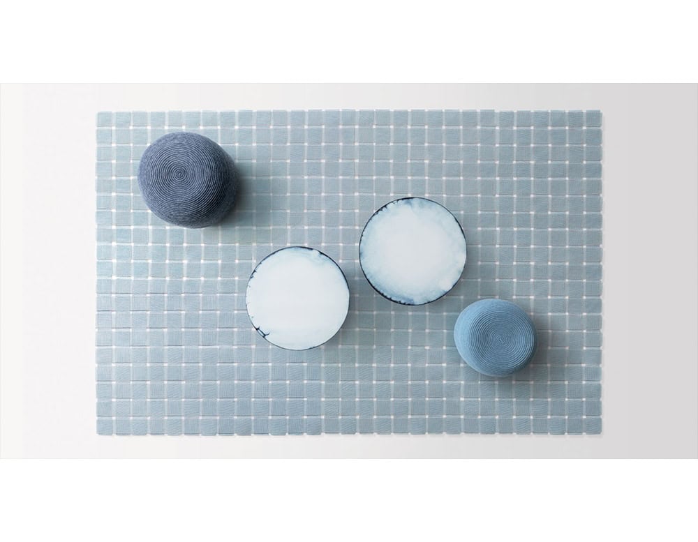 A serene composition of woven poufs and round tables rests on a patterned rug. The mix of blues brings harmony and balance to this refined design.
