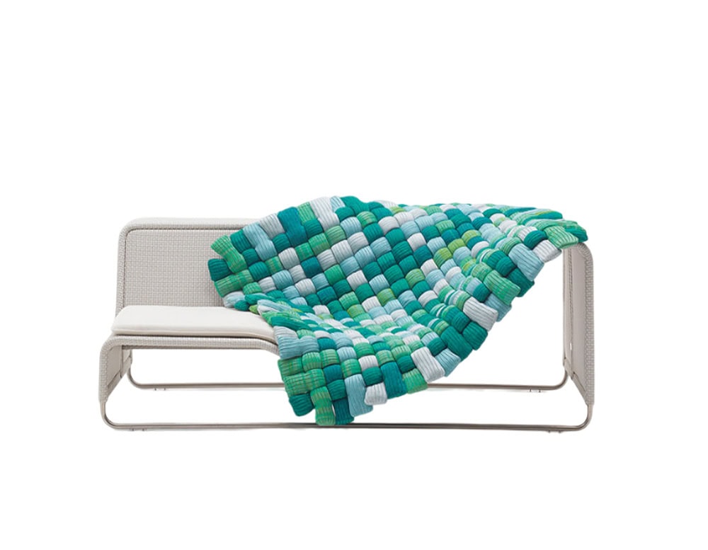 Colorful woven throw in shades of green, teal, and white, draped over a minimalist bench, adding texture and vibrancy to modern seating.