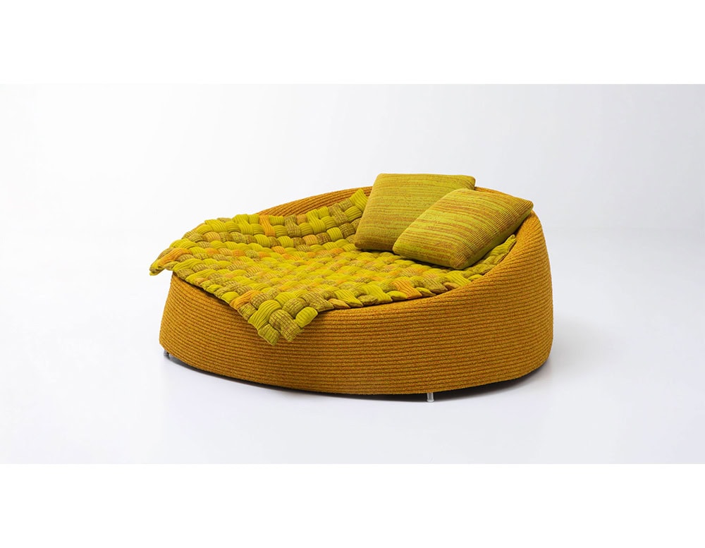Curved lounge seat in warm golden tones, paired with a bold woven throw in mustard yellow and two matching cushions for a vibrant, inviting look.