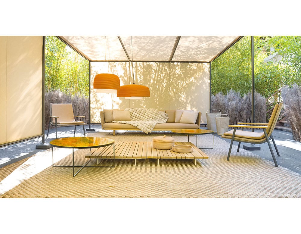 Modern outdoor lounge showcasing a sleek sofa with plush neutral cushions, paired with matching chairs and low wood tables. Bold pendant lamps add contrast, highlighting the refined craftsmanship of the set.
