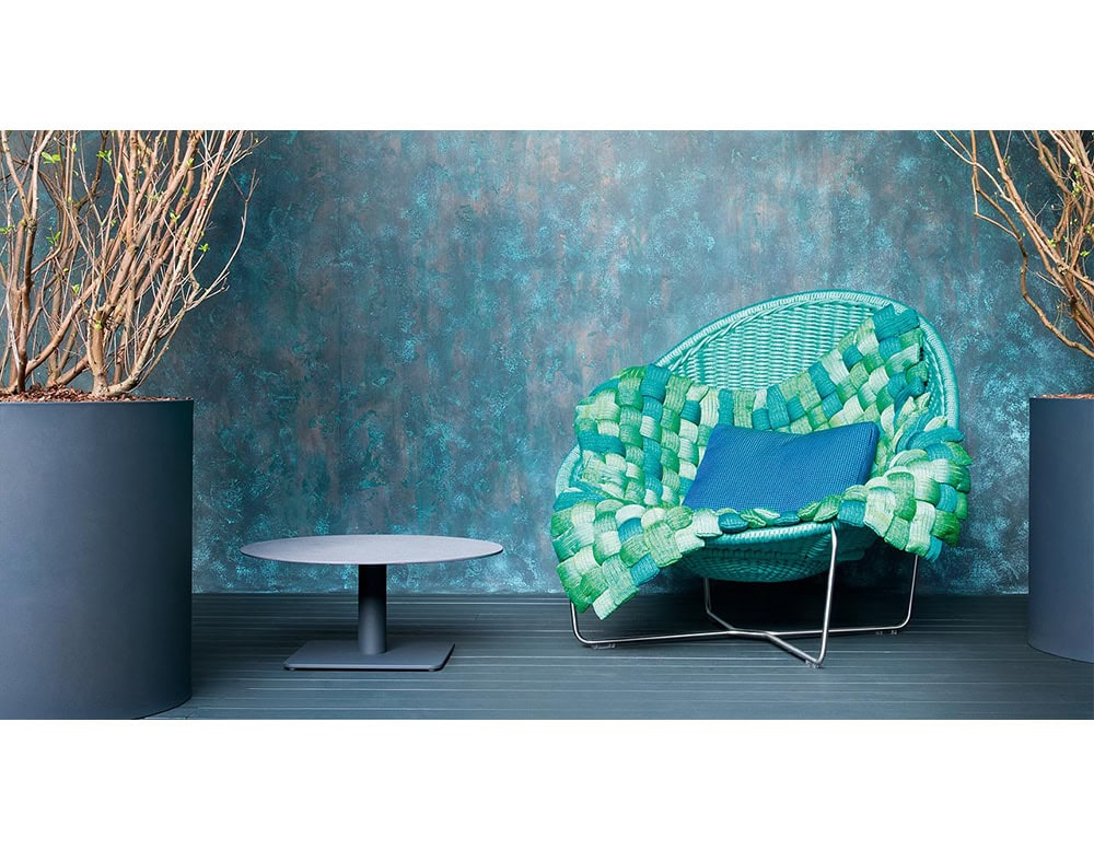 The sculptural lounge chair stands out with its woven design, layered throw, and accent pillow. A perfect mix of comfort and bold style for contemporary interiors.