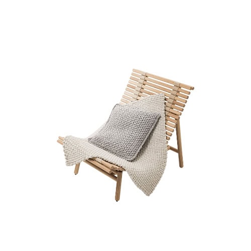 A wooden armchair with a clean slatted frame paired with a textured pillow and throw creating a natural and inviting look for relaxed seating.