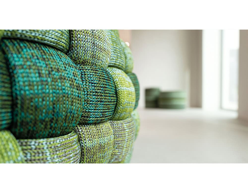 A close-up view highlights the intricate woven texture in green and blue tones, adding depth and character to the design.