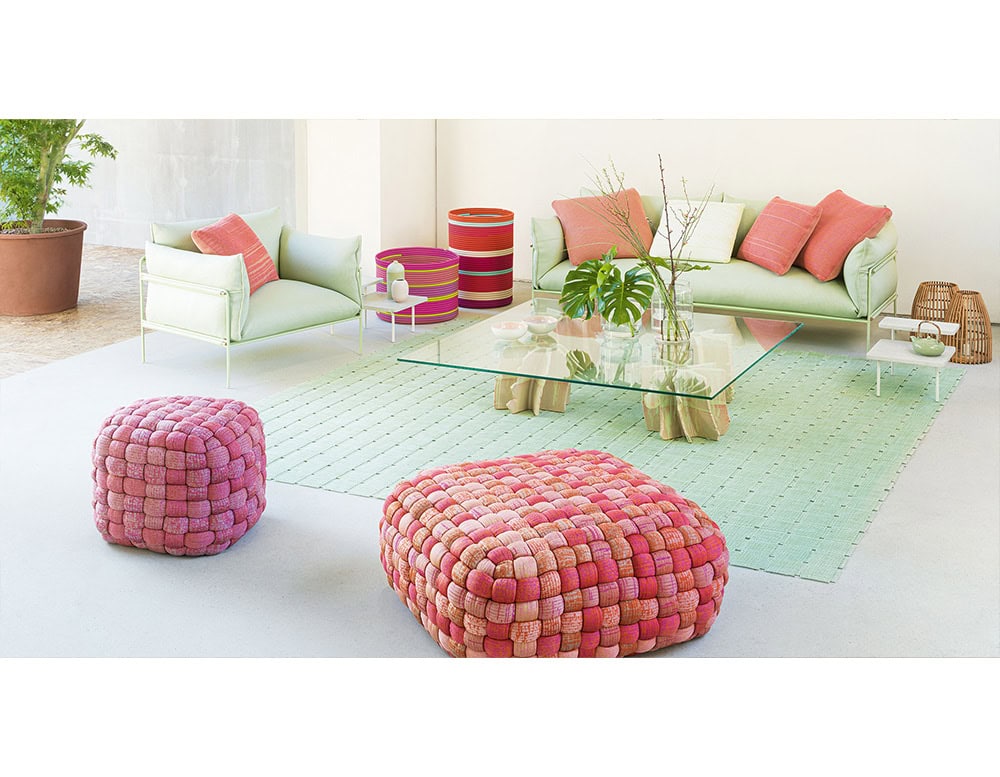Soft green sofas pair with bold woven pink poufs and pastel cushions, creating a playful contrast that brightens the space with a mix of comfort and charm.
