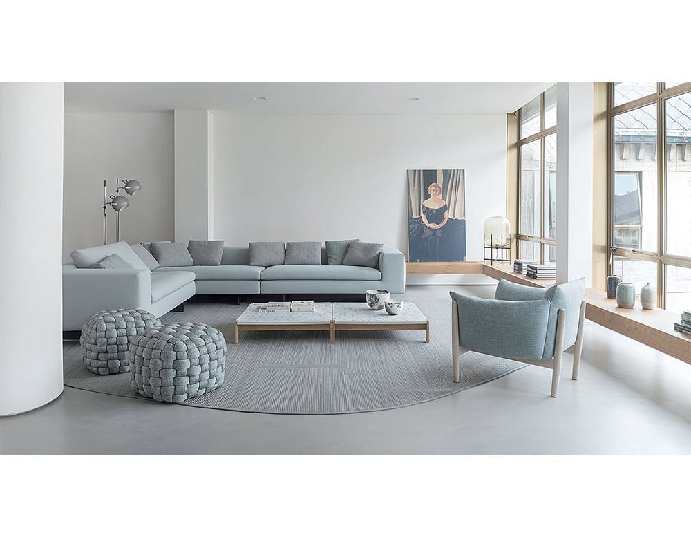 Soft woven poufs in cool gray tones anchor the living room, complementing the sleek sectional and armchair for a clean, balanced, and modern aesthetic.