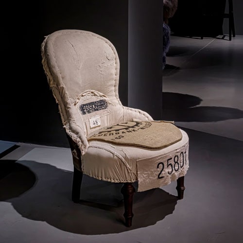 Unique chair in cream on a dark colored carpet with a dark background and a light shining on the chair