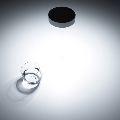 Top view of Tetatet flute light illuminating a white table with a glass of water next to it