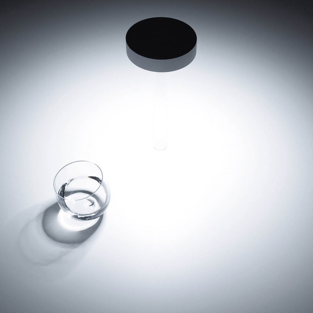 Top view of Tetatet flute light illuminating a white table with a glass of water next to it