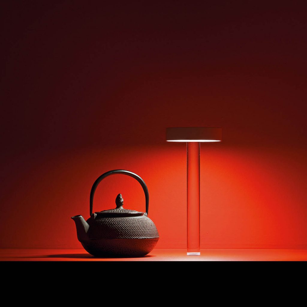 Tetatet flute light with a tea pot next to it and a red wall behind