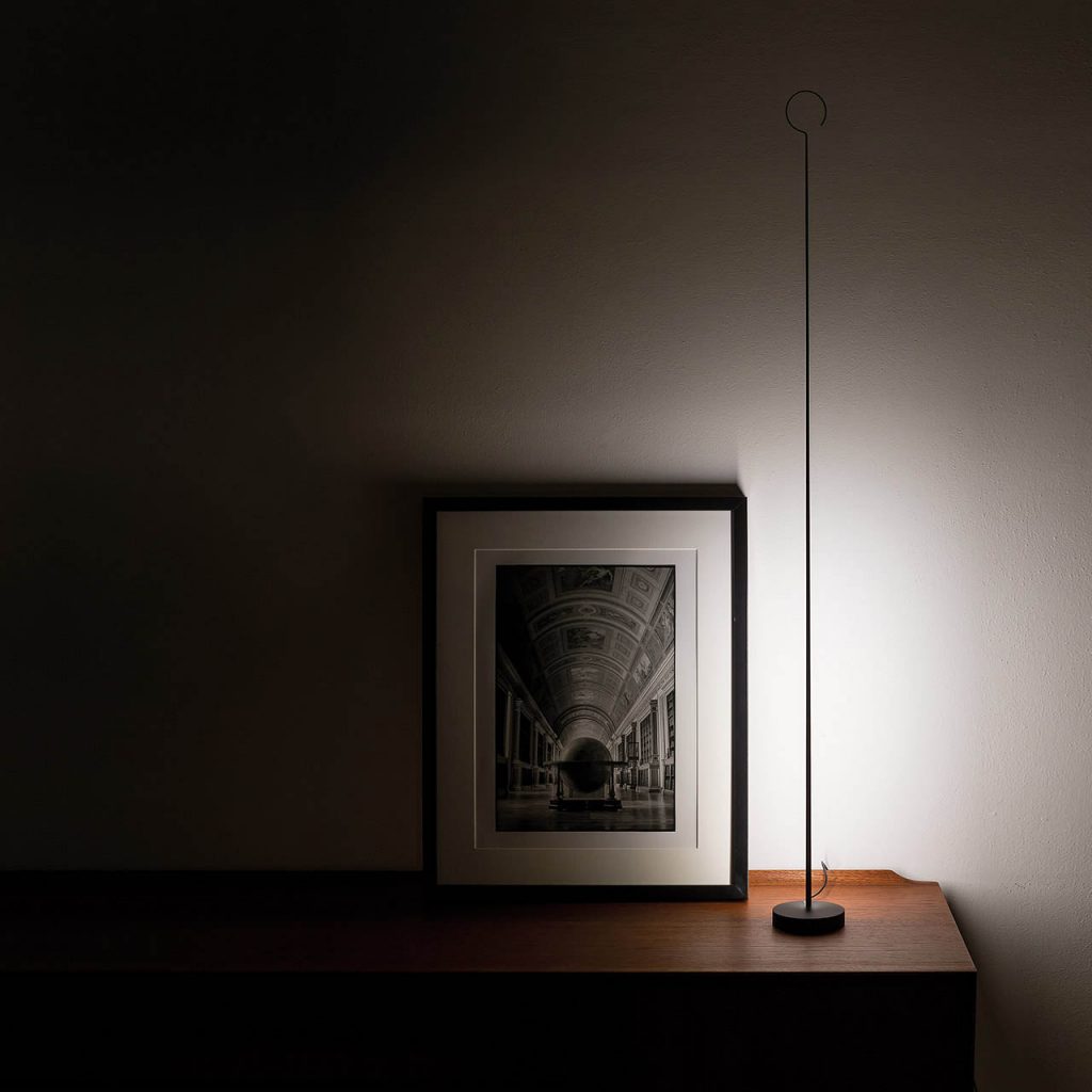 Anima light next to a framed picture shining against a white wall while on top of a table in a dark room
