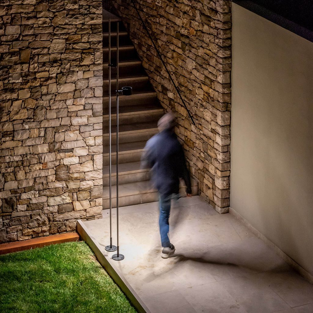Bubka outdoor lamp shining on a stone walkway with a person going towards the stone staircase in the background