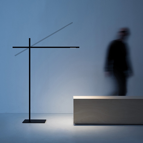 Hashi floor lamp illuminating a museum island bench with a person to the right walking away from the light