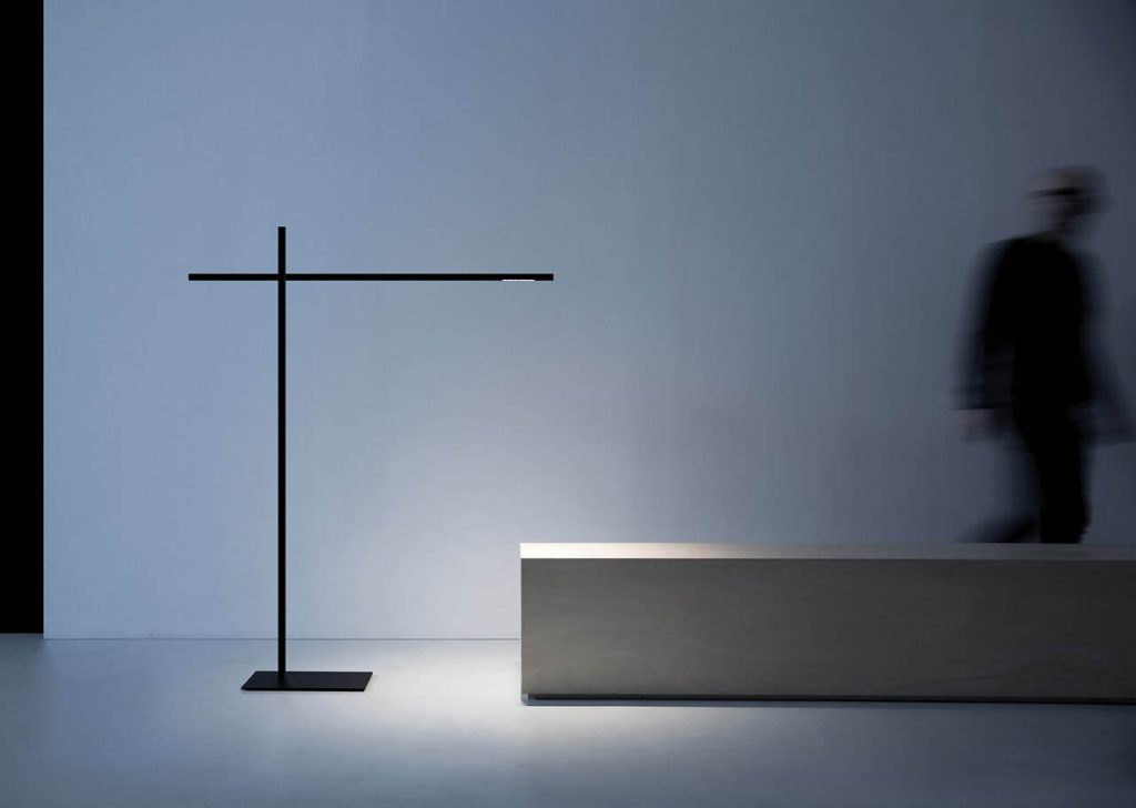 Hashi floor lamp illuminating a museum island bench with a person to the right walking away from the light