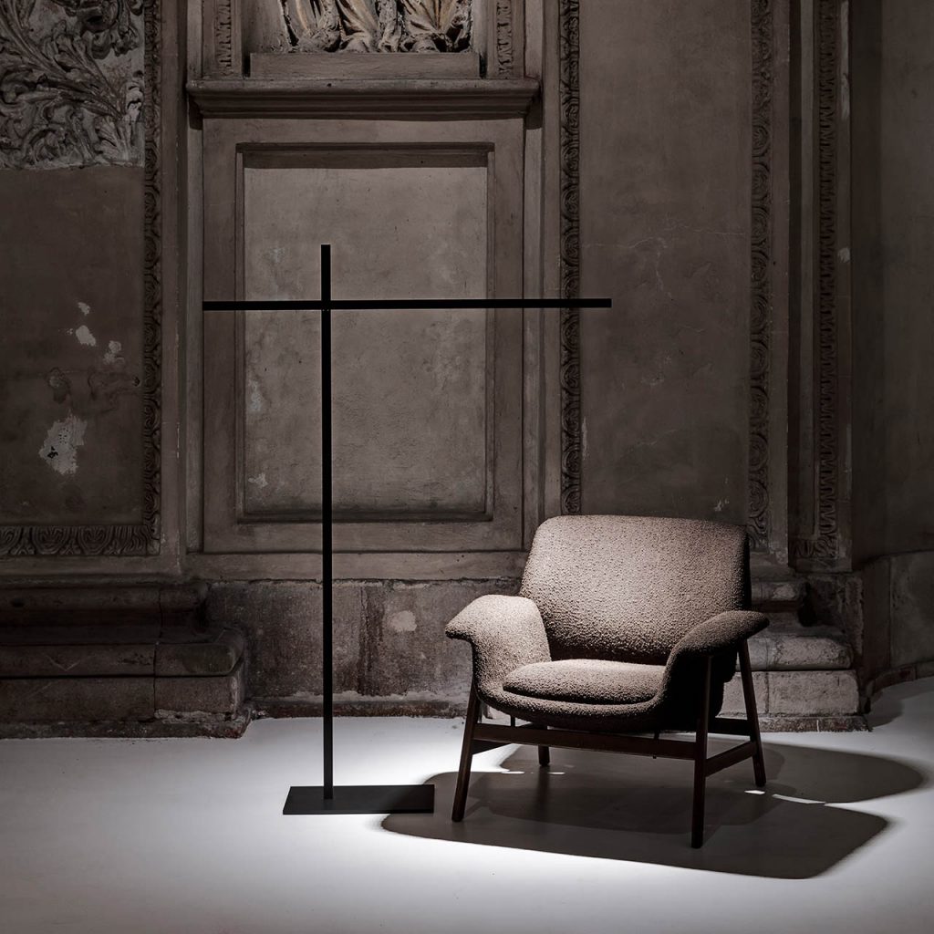 Hashi floor lamp illuminating a grey chair with a grey renaissance looking wall in the background
