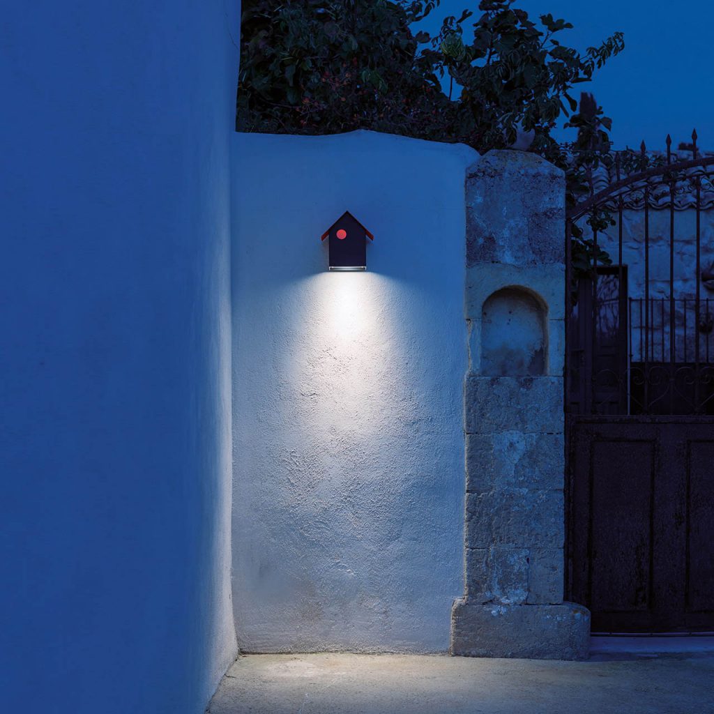 Imu light hanging on a white stone wall outside illuminating the ground
