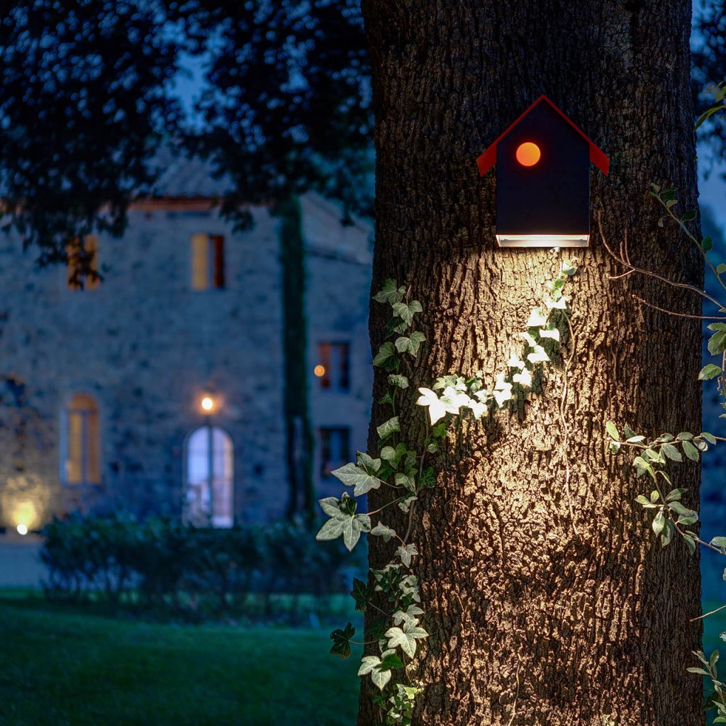 Imu light hanging illuminated on a tree with a house in the background