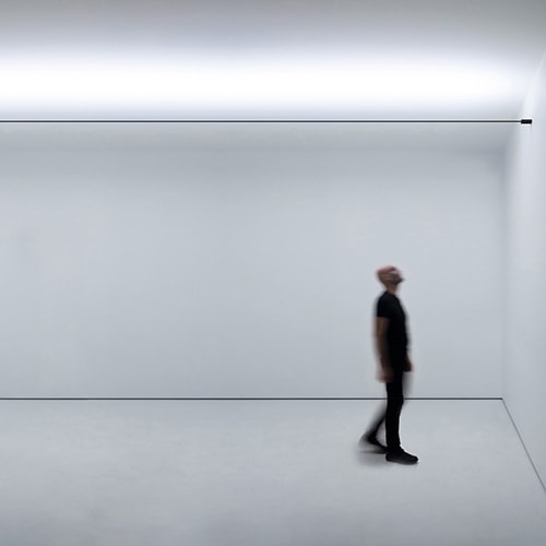 Infinito light illuminating a white room with a person underneath looking at the ceiling