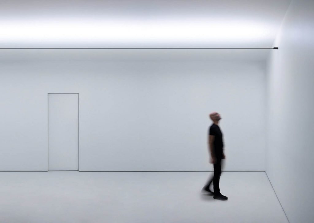 Infinito light illuminating a white room with a person underneath looking at the ceiling