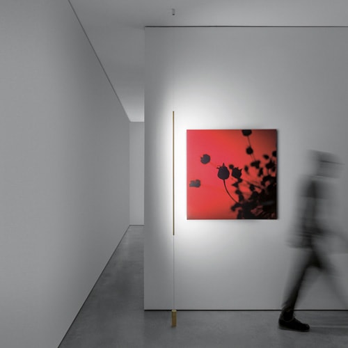 Masai light shining on a red painting with a person walking on the right side of the painting
