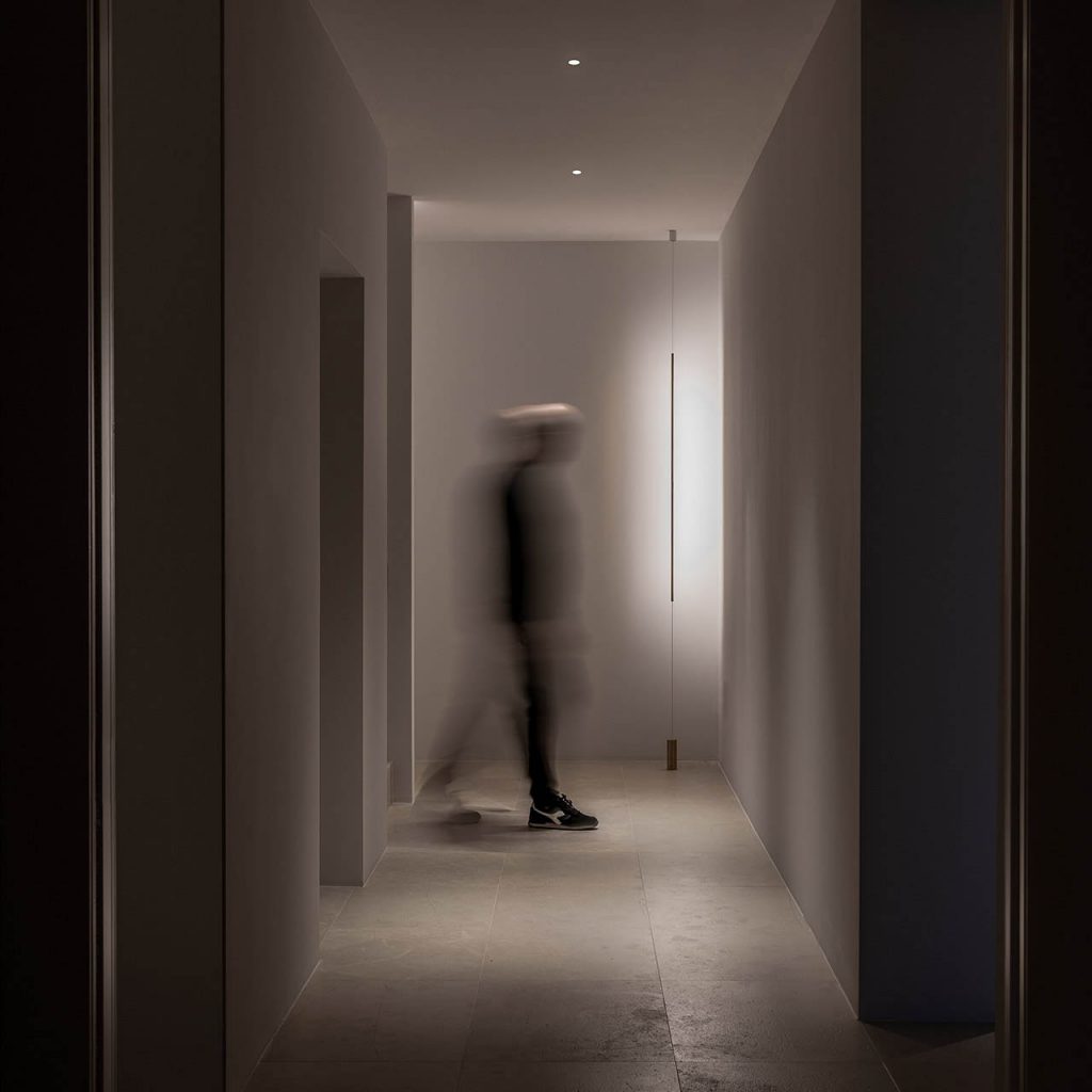 Masai light shining on a wall at the end of a hallway with a person walking across in front
