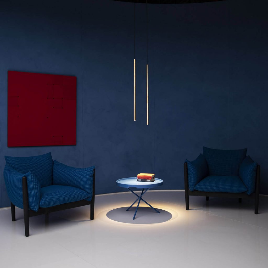 Miss suspension lamp hanging over a blue coffee table with two blue arm chairs at either side in front of a blue wall