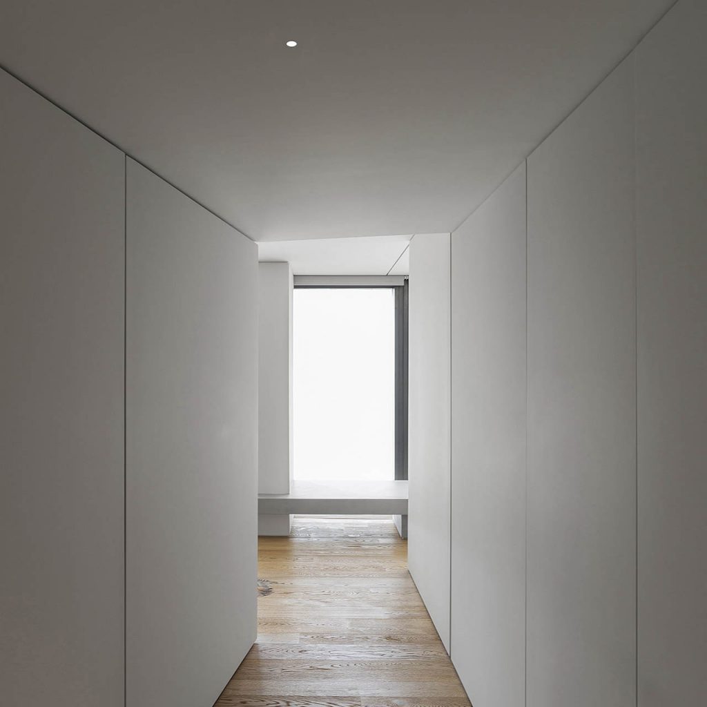 Nulla twenty five recessed lights in a white hallway with a wooden floor, a sunny window at the end of the hallway