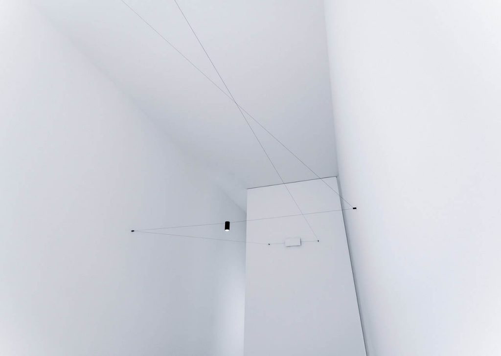 Ohm light hanging in a white walled room