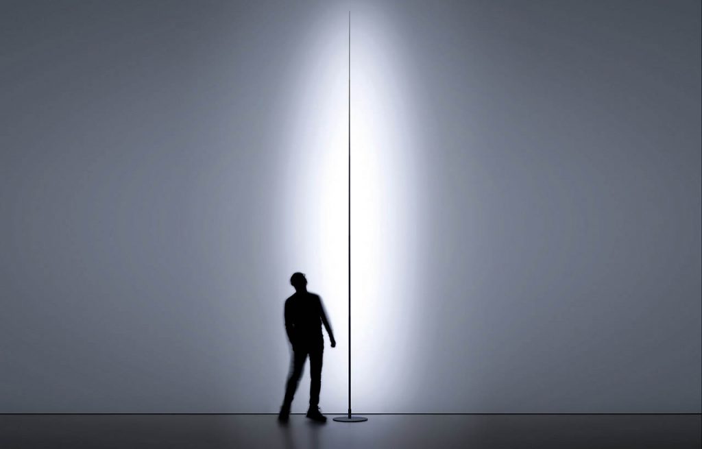 Origine light shining against a white wall with a person standing behind the light looking upwards