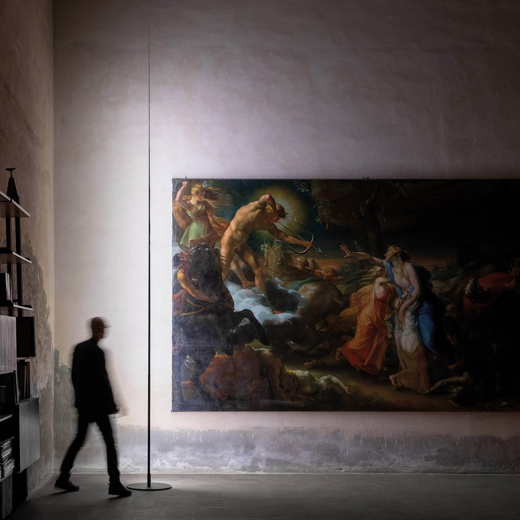 Origine light shining against a large painting with a person standing behind the light