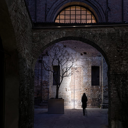Origine Outdoor shining against a grey wall with a person standing behind the light and an archway in the foreground