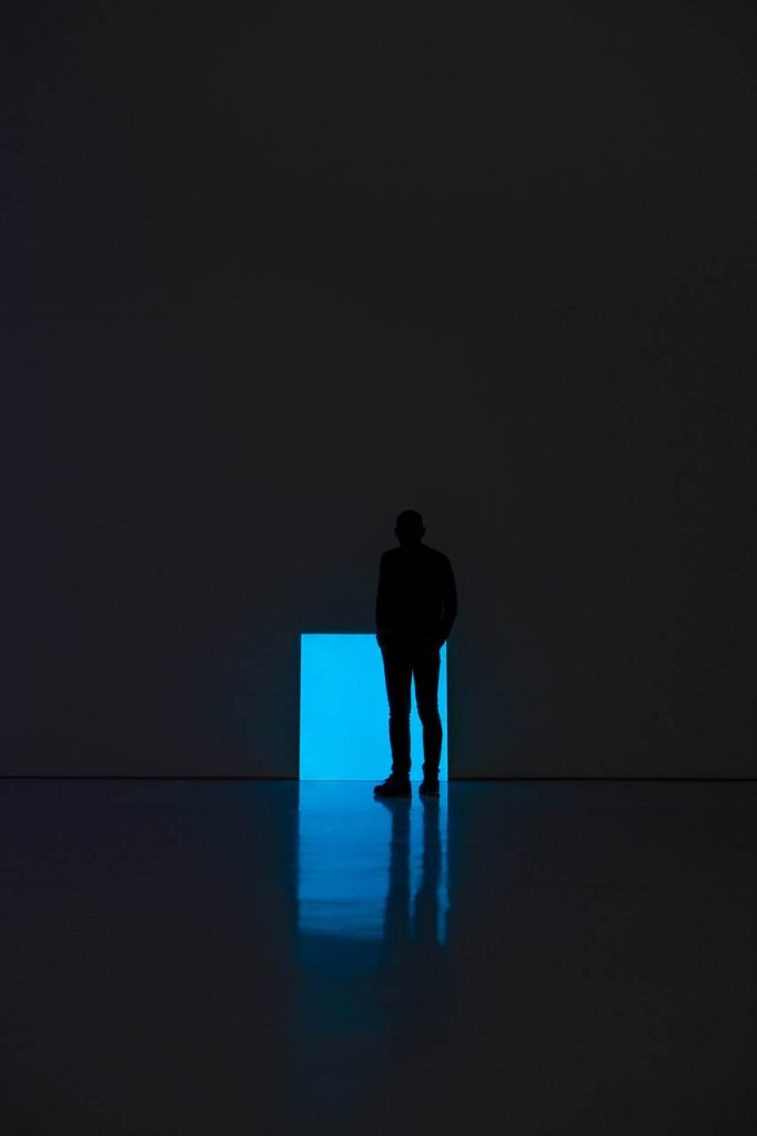 Pablo light shining in a light blue with a person standing in front in a grey walled room