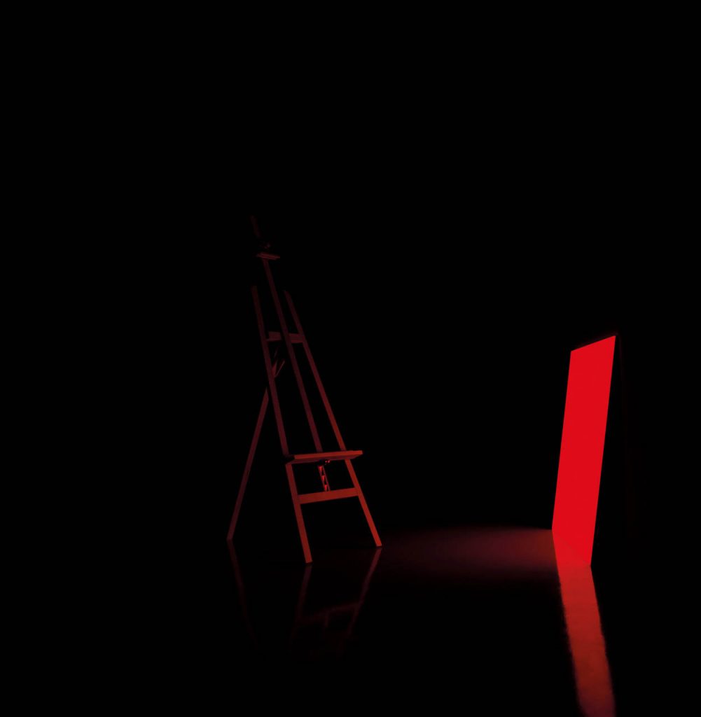 Pablo light shining in red in front of an easel in a dark room