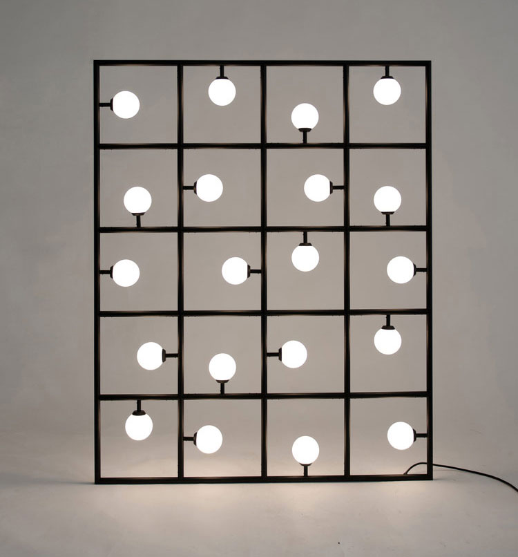 Square lights with the white bulbs illuminated in front of a darkly lit room with a grey wall behind