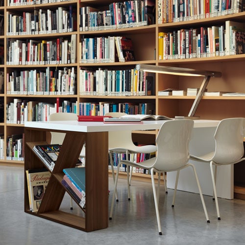 J-Table with a dark wood and white top in front of a library bookshelf