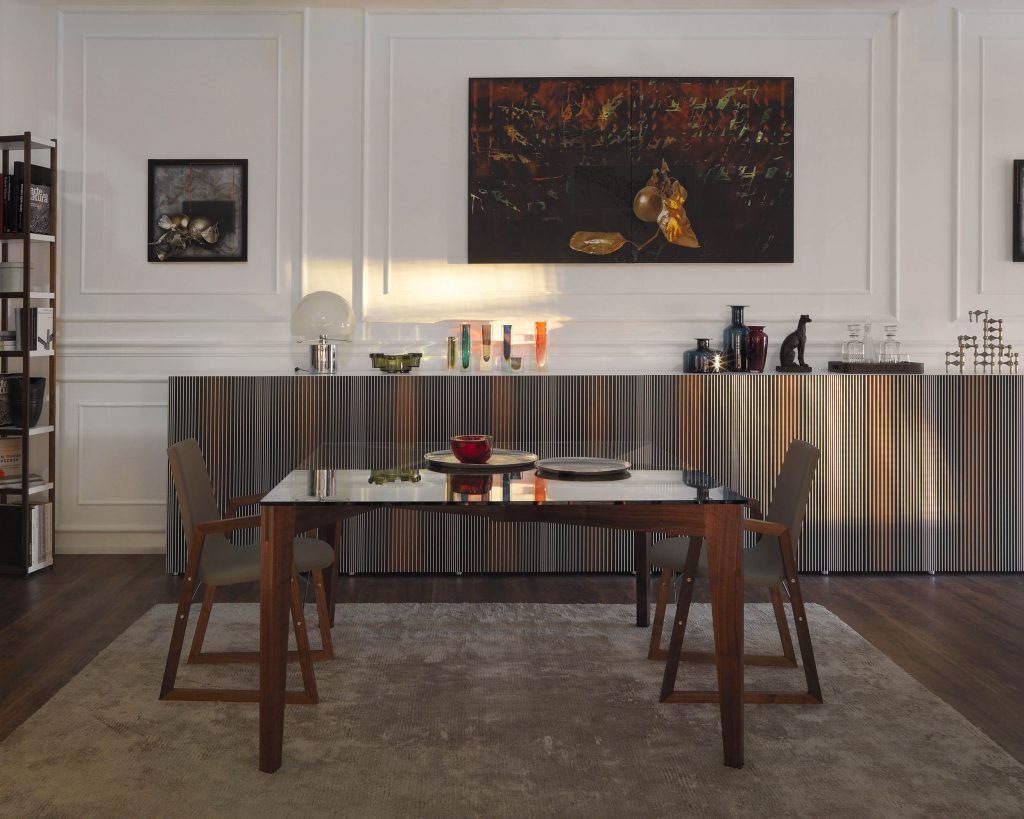 Autoreggente square glass top with chairs on the left and right side and a large cabinet in the background and a painting on the wall