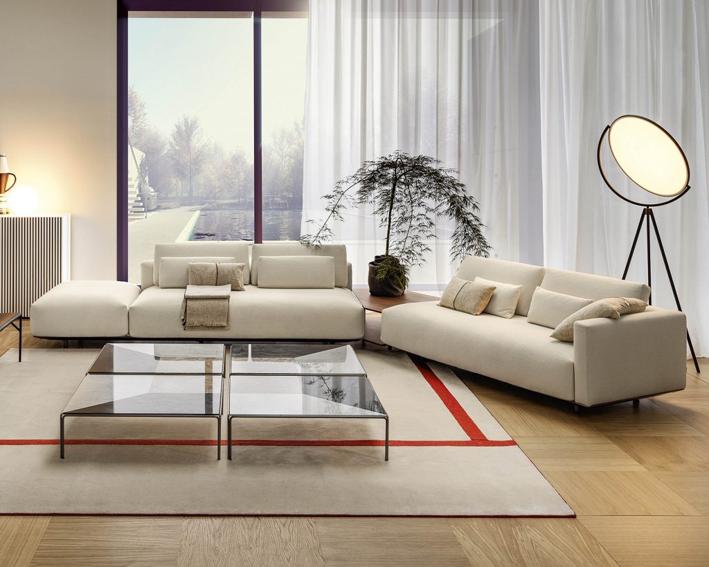 Frontal view of L-shaped cream-colored Billie on top of a cream rug with curtain covered windows in the background