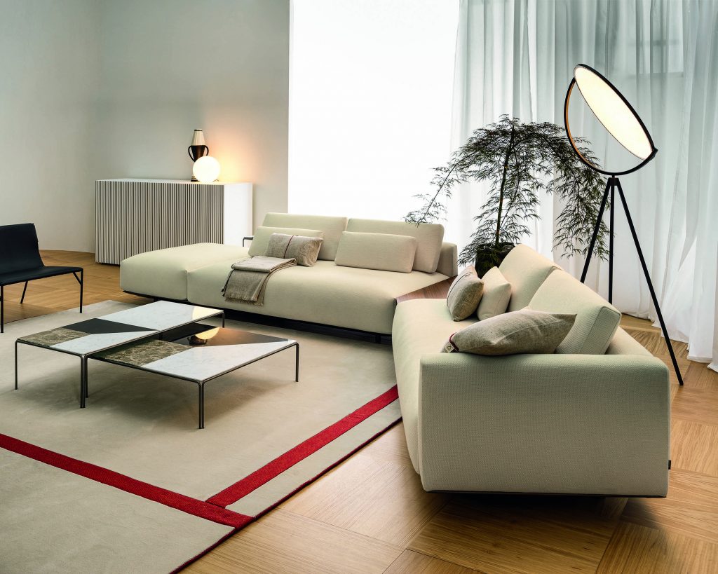 Side view of L-shaped cream-colored Billie on top of a cream rug with curtain covered windows in the background