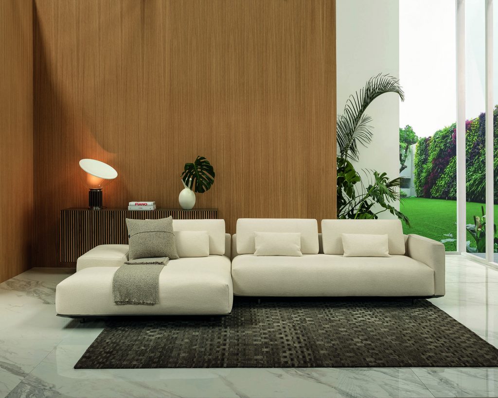 Cream colored Billie on top of a brown woven rug with a brown wooden wall behind